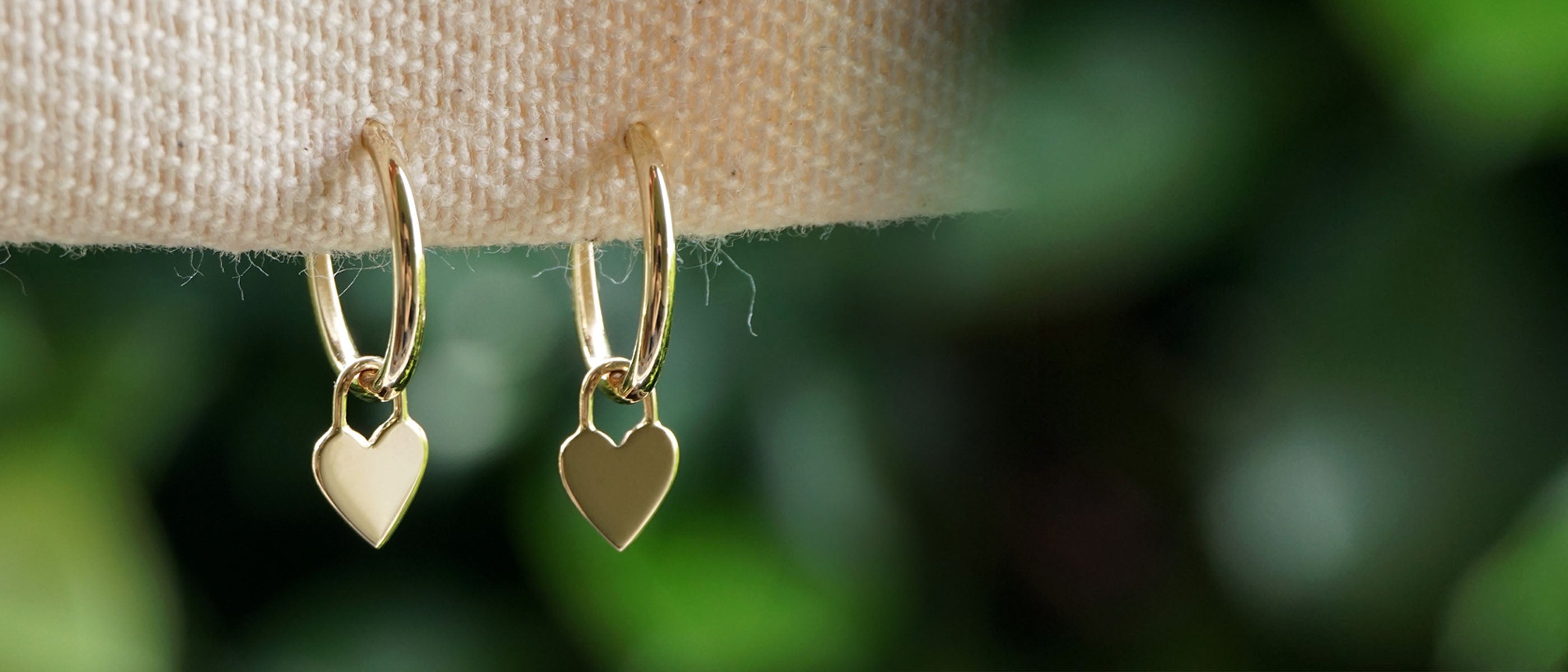 Solid gold hoop earrings with heart charms on a green background