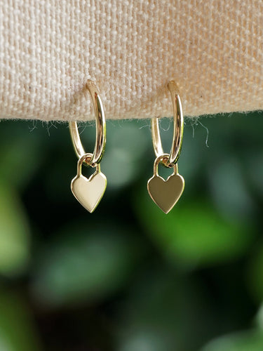 Solid gold hoop earrings with heart charms on a green background