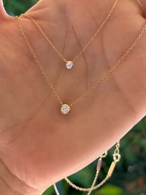 two gold necklaces with diamond pendants, 1/8 carat and 1/4 carat, respectively. Both resting in the palm of a hand.