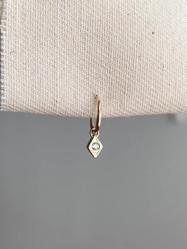 Small gold hoop with diamond-shaped charm dangling.